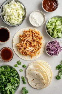 Crispy BBQ Chicken Wraps (Easy High-Protein Lunch Recipe) 5 Flatlay of ingredients for BBQ chicken wraps including shredded chicken, barbecue sauce, tortillas, coleslaw mix, lettuce, cheese and ranch dressing.