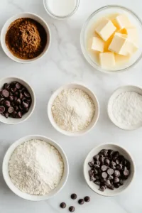 Ingredients for edible cookie dough for one including flour, butter, brown sugar, vanilla extract, milk, and chocolate chips arranged on a kitchen counter.