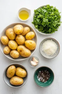 Ingredients for air fryer smashed potatoes including baby potatoes, olive oil, garlic, herbs, salt, and pepper arranged on a kitchen countertop.