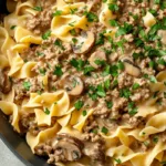Creamy ground beef stroganoff with egg noodles in a skillet, garnished with parsley