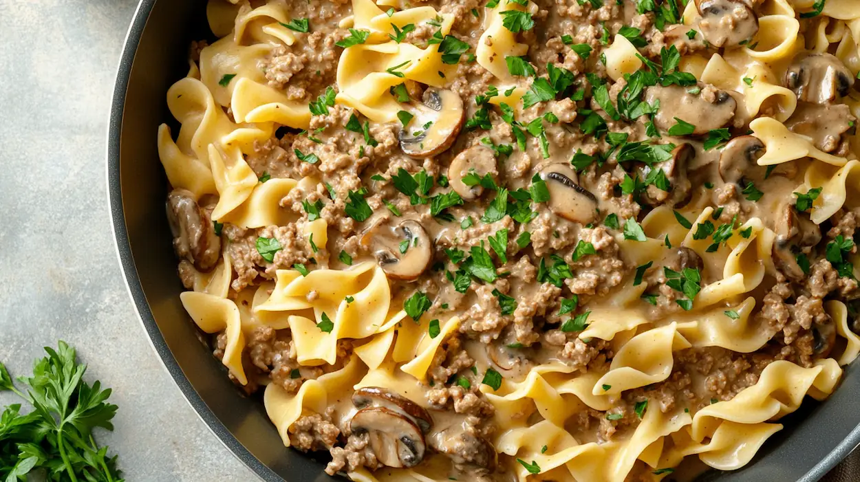 Creamy ground beef stroganoff with egg noodles in a skillet, garnished with parsley