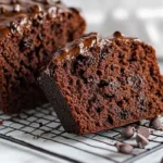 A sliced loaf of double chocolate zucchini bread topped with chocolate chips on a cooling rack.
