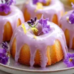 Mini lemon bundt cakes with glossy lavender glaze, lemon zest, and edible flowers on a serving plate in natural light.