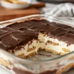 Slice of no-bake chocolate eclair dessert with creamy vanilla pudding layers, softened graham crackers, and glossy chocolate topping