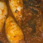 Cleaned squid, cooked rice, shrimp, onion, garlic, tomatoes, spices, parsley, and olive oil arranged on a white counter at night