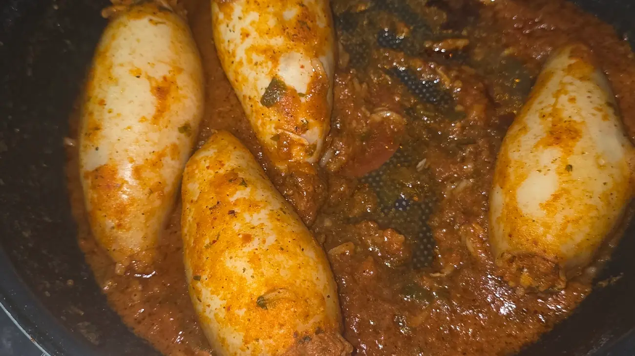 Cleaned squid, cooked rice, shrimp, onion, garlic, tomatoes, spices, parsley, and olive oil arranged on a white counter at night