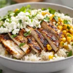 Street Corn Chicken Rice Bowl Recipe Street corn chicken rice bowl with sliced seasoned chicken, cilantro lime rice, and creamy charred corn topping in a modern American kitchen.