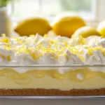 Creamy lemon icebox dessert in a glass dish topped with whipped cream, lemon zest, and a cookie crust.